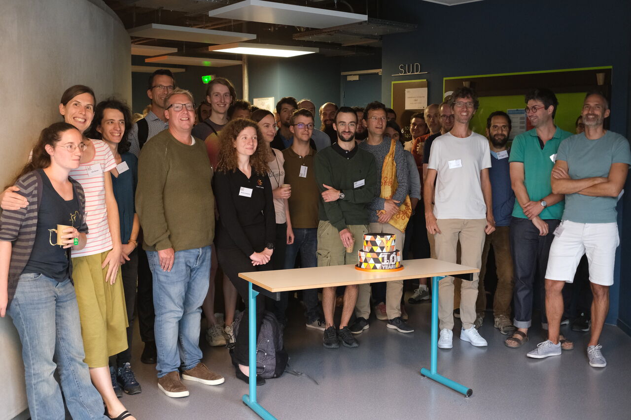 Group photo around the birthday cake.  By Christopher Baines, CC0.